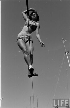 an old photo of a woman hanging on to a pole