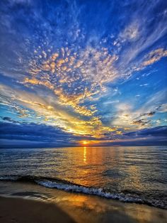 the sun is setting over the ocean with clouds in the sky and water on the beach