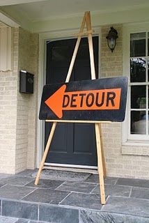 an orange detour sign sitting on top of a wooden easel in front of a house