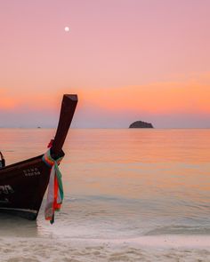 the boat is tied up on the beach at sunset with an island in the background