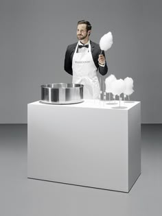 a man in an apron is standing behind a white counter with pots and pans on it