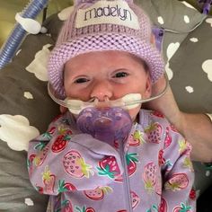 a baby with a pacifier in its mouth wearing a pink hat and purple pajamas