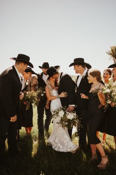 a group of people standing next to each other wearing black hats and dress clothes with bouquets