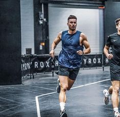 two men running on a tennis court in the middle of an indoor area with garage doors behind them