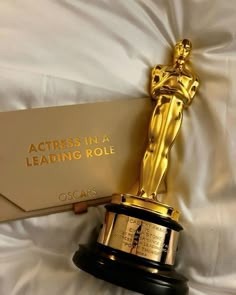 an oscar statue sitting on top of a bed next to a paper sign that says actress in a leading role