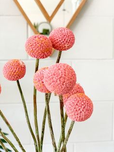 some pink flowers are in a vase on a table next to a mirror and a plant