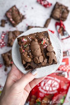 a person holding a plate with some brownies on it and candy in the background