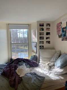 an unmade bed in front of a window with pictures on the wall above it