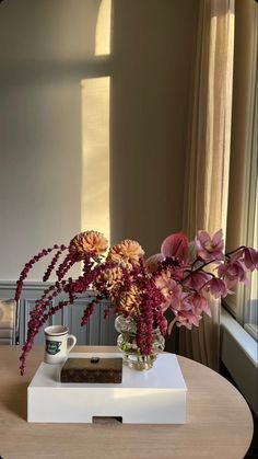 a vase filled with flowers sitting on top of a wooden table next to a window