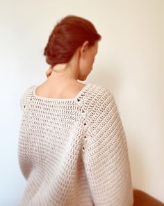 a woman wearing a white crochet sweater looking off into the distance with her back to the camera