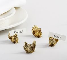 four small gold turkey napkin holders on a white table with place cards in front of them