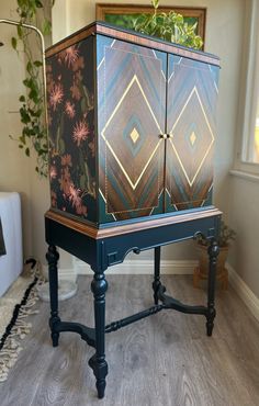 a blue cabinet with flowers painted on it in a living room next to a window