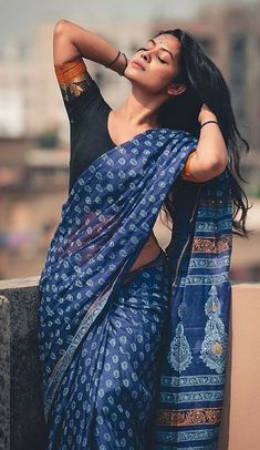 a woman in a blue sari leaning on a wall with her arms behind her head