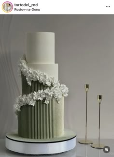 a three tiered green and white wedding cake with flowers on the top, next to two candles