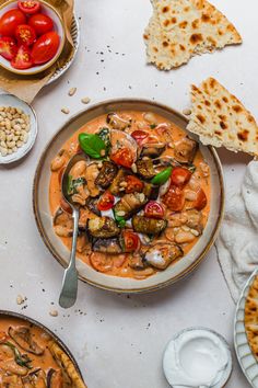 an overhead view of a bowl of soup with bread and tomatoes on the side, along with other dishes