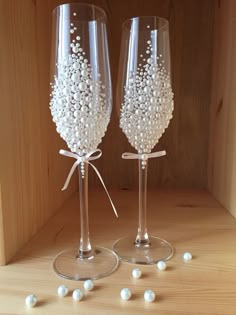 two wine glasses decorated with pearls and bows on top of a wooden table next to each other