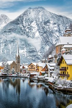 snow covered mountains surround a small village in the middle of a body of water with buildings on both sides