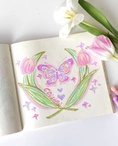 an open book with flowers and butterflies on the pages, next to some crayon markers