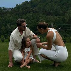 a woman and two children sitting on the grass with an adult standing next to them