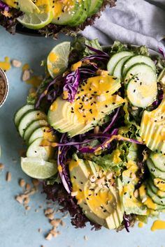 a salad with cucumber, lettuce and cheese on it next to a bowl of dressing