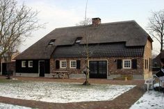 an old brick house with a thatched roof in the middle of snow covered ground