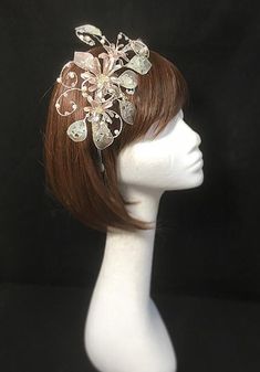 Delicate silver beige fascinator perfect for the guest who wants something fairly understated. This design is a beautiful selection of glass effect leaves and flowers clustered together and set onto a fine comfort base tiara band. As with all our designs, this piece can be made exact to the image or in any colour combination to match in with your outfit. If a specific colour is required customers can message over an image of their outfit and accessories, or if time allows customers are always we Elegant Cream Headpiece For Gift, Beige Hair Accessories For Wedding, Beige Wedding Headband, Beige Headband For Party, Beige Headband For Wedding, Beige Headband Hair Accessories For Wedding, Beige Fascinator With Handmade Flowers For Party, Elegant Silver Headband Fascinator, Beige Party Fascinator With Handmade Flowers