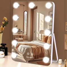 a mirror with lights on top of it next to a bed and vase filled with flowers