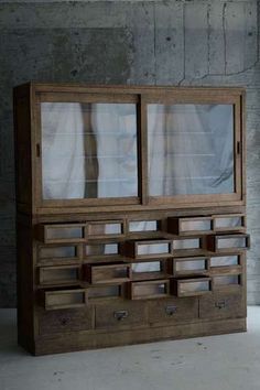 an old wooden cabinet with glass doors and drawers on the bottom, in front of a concrete wall