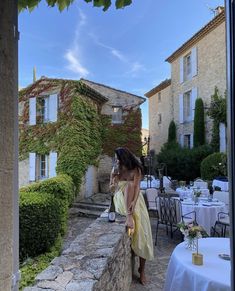 a woman in a yellow dress standing on a stone wall next to tables and chairs