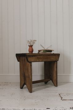 a small wooden table with a vase and book on it next to a white wall