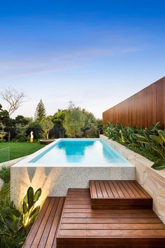 a wooden deck next to a swimming pool in the middle of a lush green yard