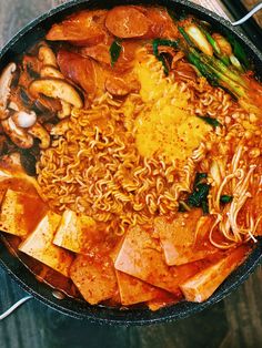 a pan filled with noodles and vegetables on top of a wooden table