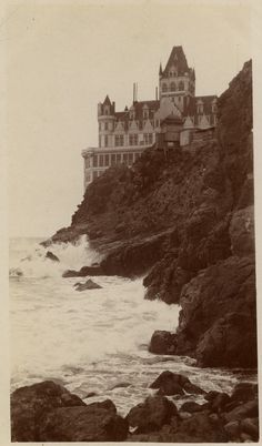 an old black and white photo of a castle by the ocean with waves coming in