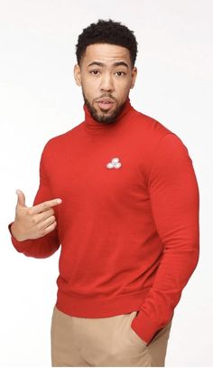 a man in a red turtle neck sweater pointing to the left with his finger up