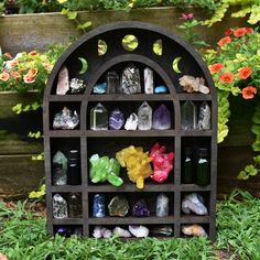 a shelf with many different types of rocks and stones on it in front of some flowers