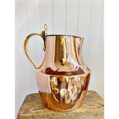 a copper colored pitcher sitting on top of a wooden table next to a white wall