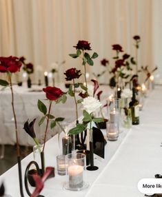 there are many vases with roses in them on the long table, along with candles