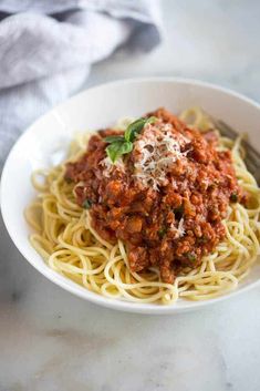 a white bowl filled with spaghetti and sauce on top of a marble countertop next to a napkin