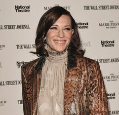 a smiling woman standing in front of a wall with the words national theatre on it