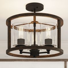 This 3-light semi-flush mount illuminates any room with a warm, ambient glow. The central candelabra fixture as well as the open cylindrical frame are crafted from steel with a two-tone finish of black and a wood-look hue for a mix of modern and farmhouse. Three 60W max bulbs (sold separately) are surrounded by clear glass cylindrical shades that reflect light throughout your space. With a hanging height of 14", this mount is ideal for smaller areas with low ceilings. The dimmer switch can also Rustic Dining Room Lighting Over Table, Ski Cottage, Semi-flush Mount Lights, Farmhouse Light Fixtures, Entryway Lighting, Low Ceilings, Flush Mount Lights, Glass Ceiling Lights, Austin Design