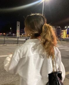 a woman walking down the street at night with her hand in her pocket and purse