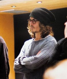 a man with long hair wearing glasses and a beanie standing in front of other people