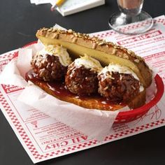 a meatball sandwich on a bun with sauce and toppings sits on a table next to a drink