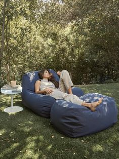 a woman laying on top of a blue bean bag chair next to a white table