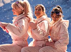 three women in pink outfits sitting on top of a snow covered mountain