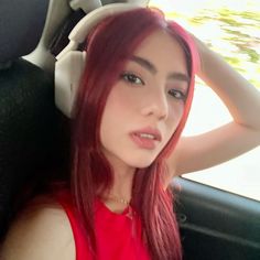 a woman with red hair wearing headphones sitting in a car looking at the camera