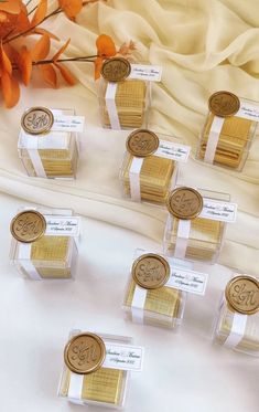 small clear boxes with gold wax seals and ribbons on a white table cloth next to orange flowers