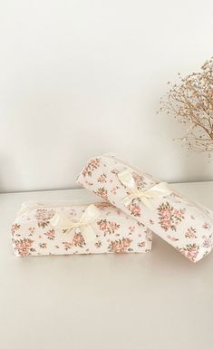 two wrapped presents sitting on top of a table next to a vase with dried flowers