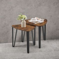 two wooden tables with metal legs on carpeted floor next to concrete wall and plant