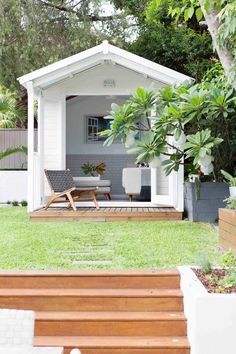 a small white house sitting on top of a lush green field next to a tree